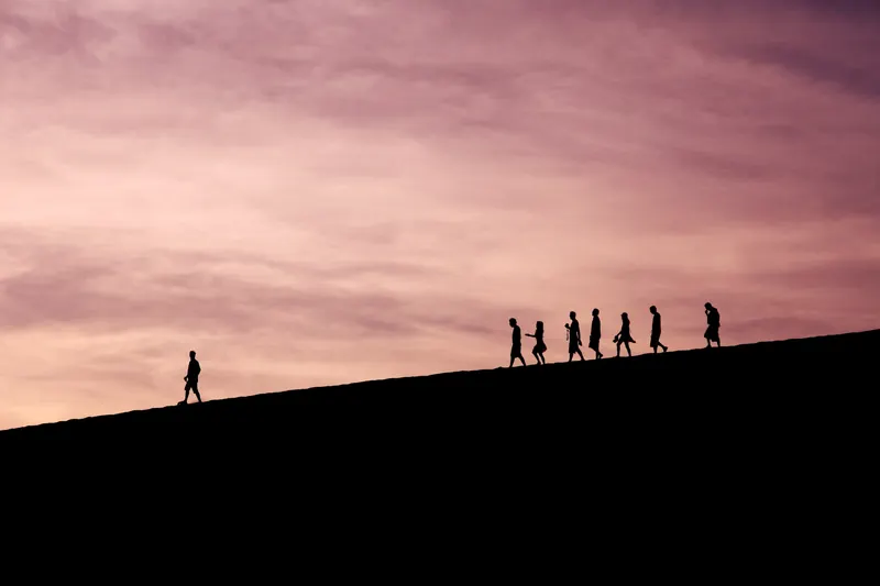 Un gruppo di persone che cammina in fila su una collina al tramonto